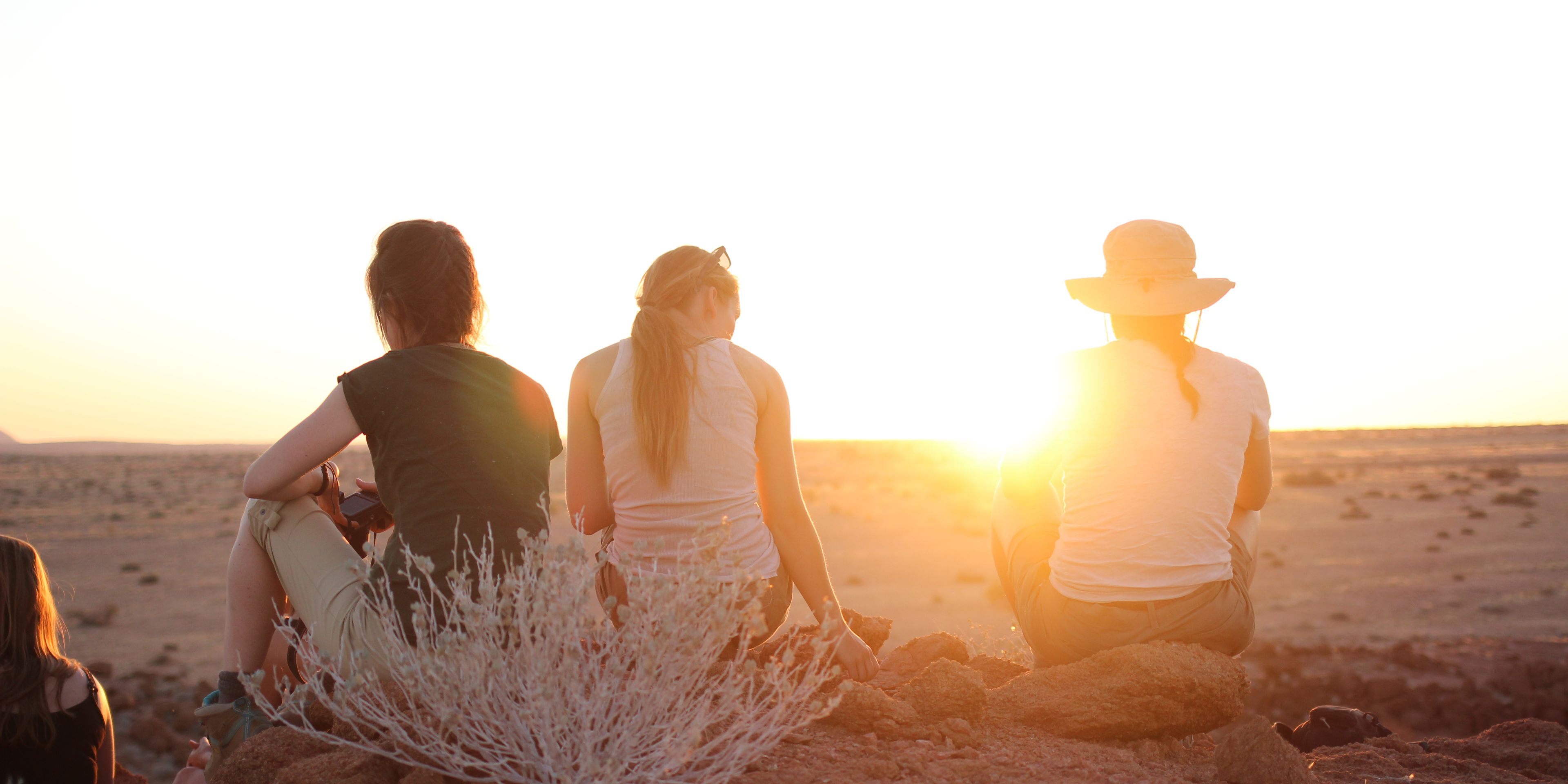 Freiwillige Helfer in Namibia sitzen auf einem Huegel und geniessen den Sonnenuntergang.