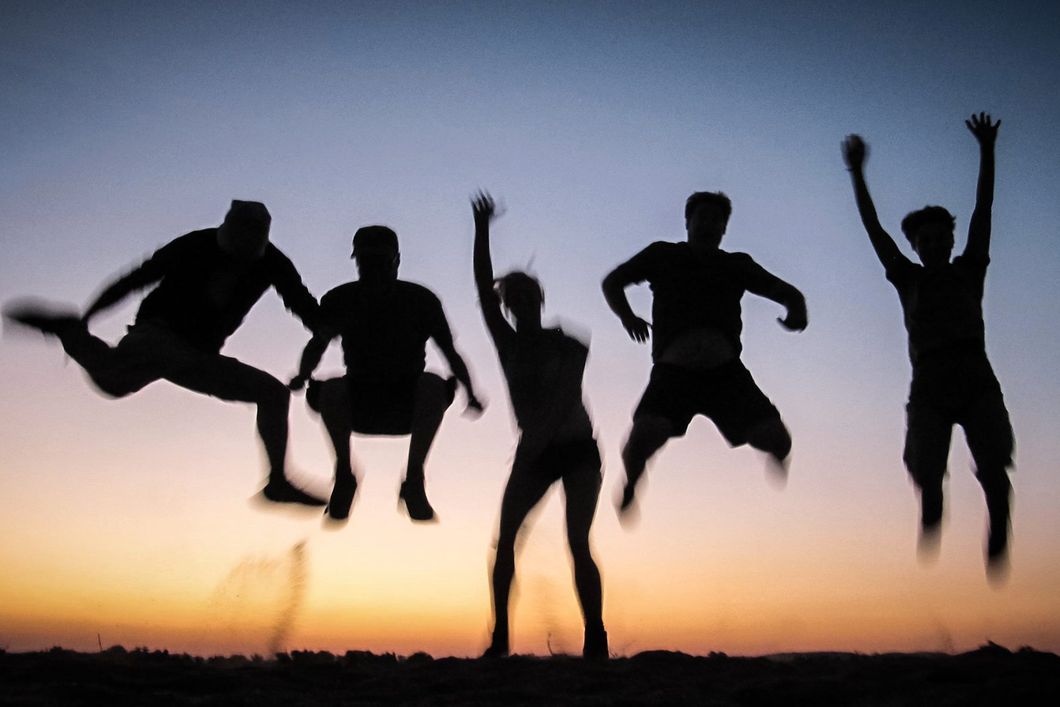 Fuenf Teilnehmer springen vor Freude ueber den Safari Trip im Abendlicht in die Luft