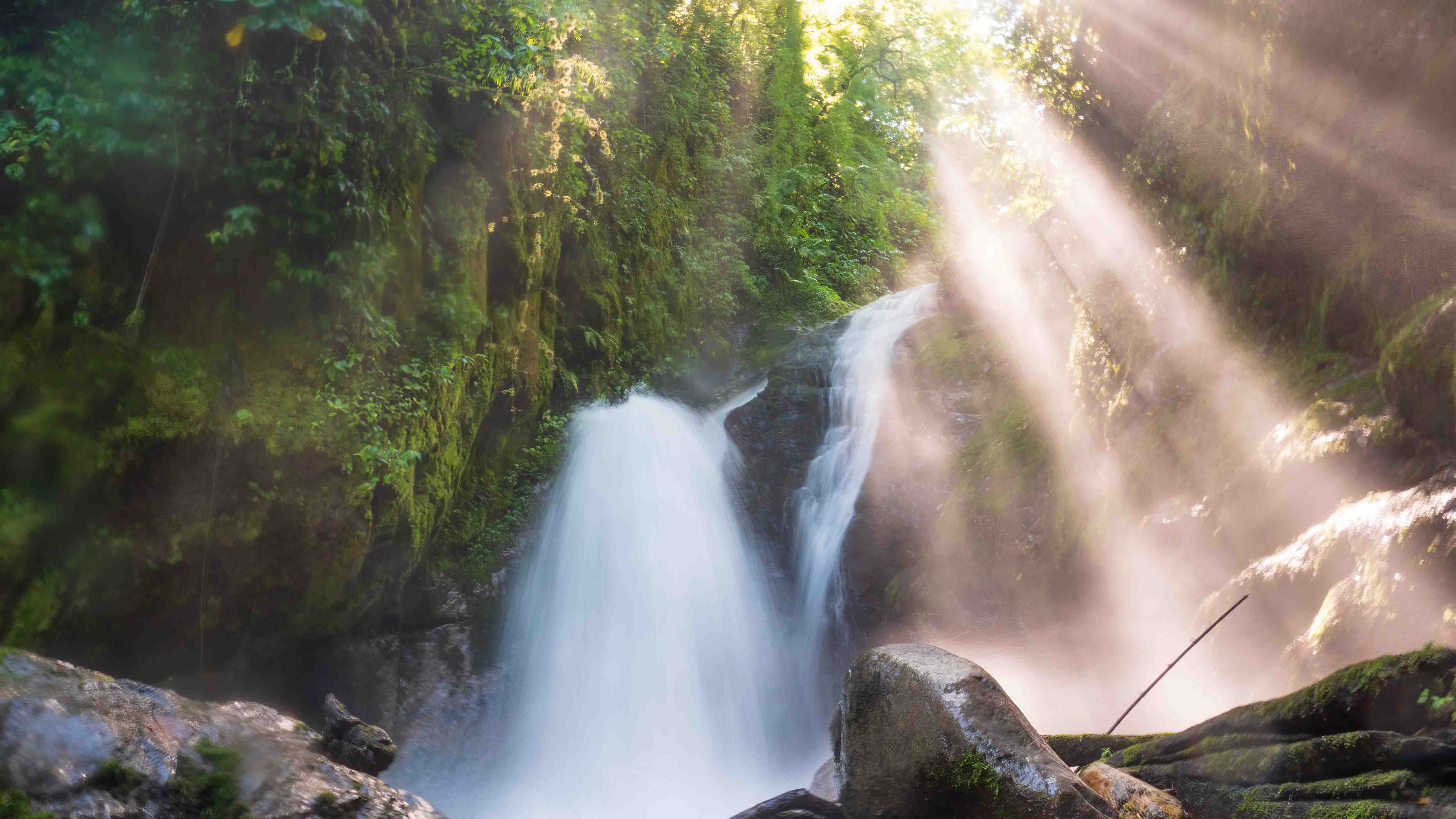 Zu sehen ist ein Wasserfall aus dem neotropischen Wald in Costa Rica. Aufnahme aus niedrigem Winkel lässt den Wasserfall mächtig wirken und fängt die Sonnenstrahlen, die durch den dicht bewachsenen Wald fallen, ein.